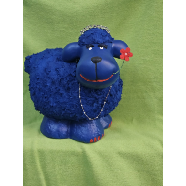Kräftig blaue, rundliche Schaffigur mit roter Blume am Ohr, kleinen roten Akzenten und einer Halskette vor grünem Hintergrund.