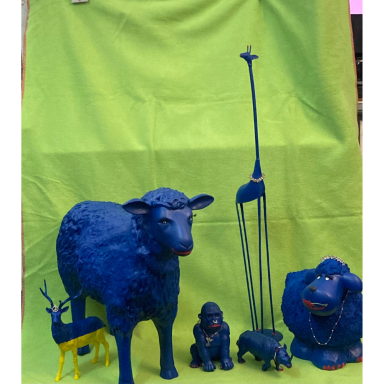 Gruppe verschieden großer blau gestalteter Tierfiguren, darunter eine Giraffe, ein Schaf, ein Affe, ein Nashorn und ein Hirsch, vor grünem S