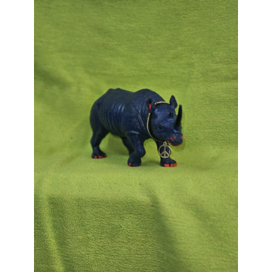 Kleine dunkelblaue Nashornfigur mit zwei Hörnern, roten Akzenten und einer goldfarbenen Friedenszeichen-Kette vor grünem Hintergrund.