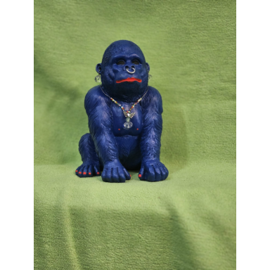 Sitzende dunkelblaue Gorillaskulptur mit kräftigen Armen, roten Lippen, roten Zehennägeln und goldfarbener Halskette vor grünem Hintergrund.