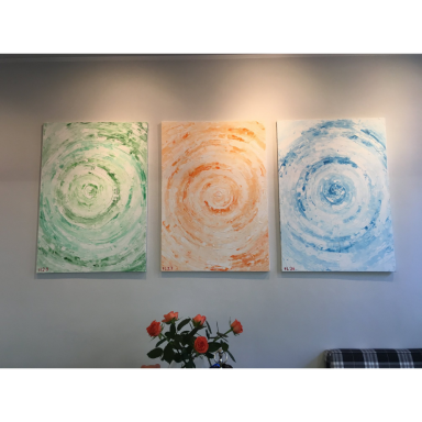 Drei abstrakte Gemälde mit grünen, orangefarbenen und blauen Kreisstrukturen hängen nebeneinander an einer grauen Wand.